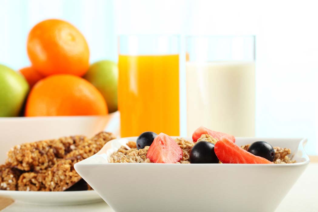 A bowl of cereal, granola, fruit and orange juice on a table
