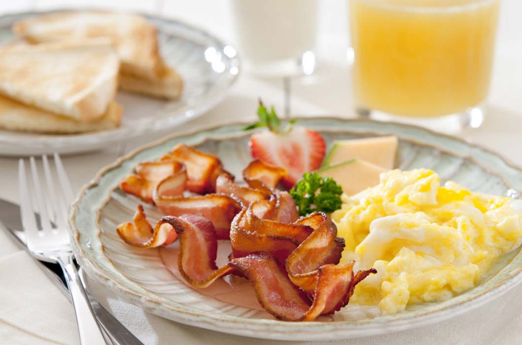 A plate of eggs and bacon with orange juice
