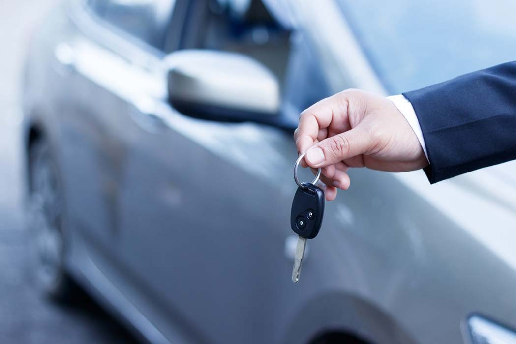 A hand holding a car key in front of a car